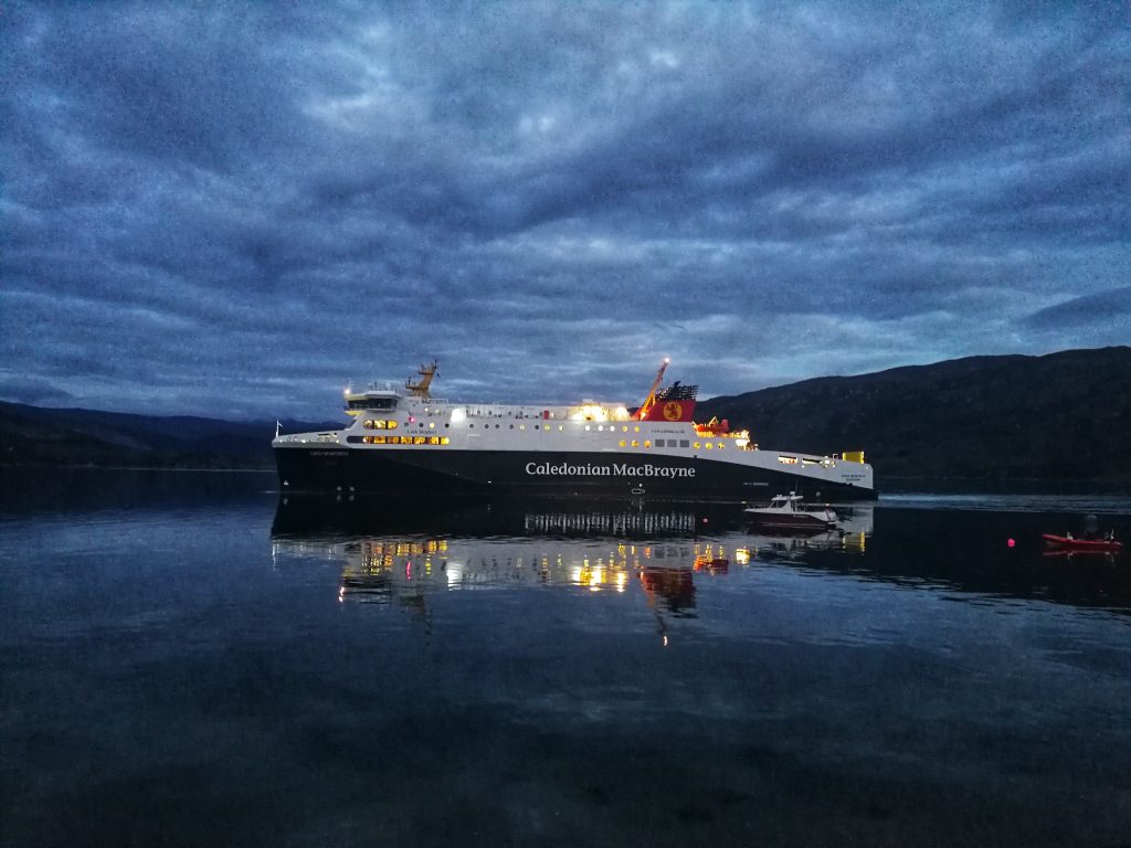 Un traghetto Caledonian MacBrayne al porto, con le luci riflesse sull’acqua